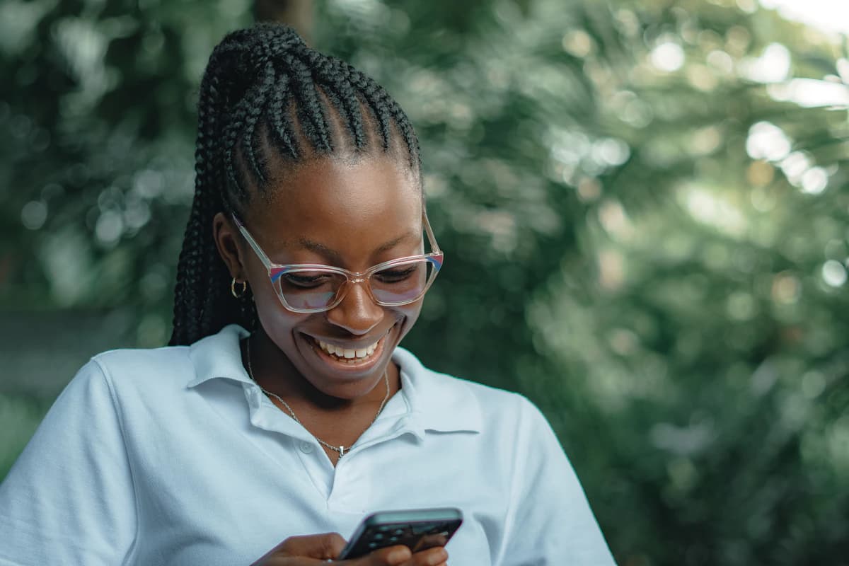 A woman smiling as she looks at her phone.